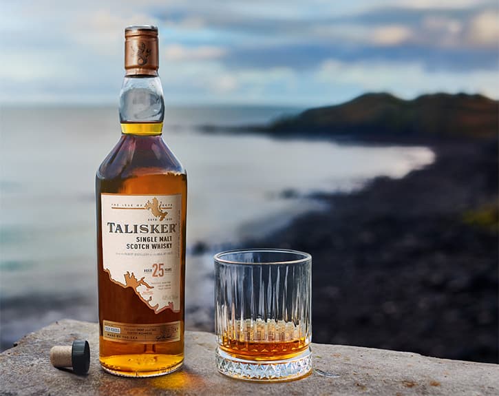 Talisker 25 Year Old and a glass of whisky beside the bottle on a coast