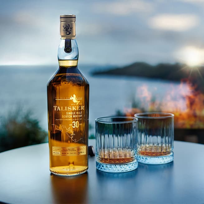 Talisker 30 Year Old on a table with two glasses of whisky beside the bottle on the coast
